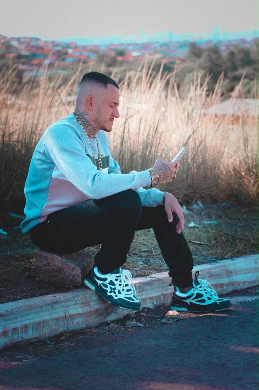 Lucas sentado na rua, olhando o celular